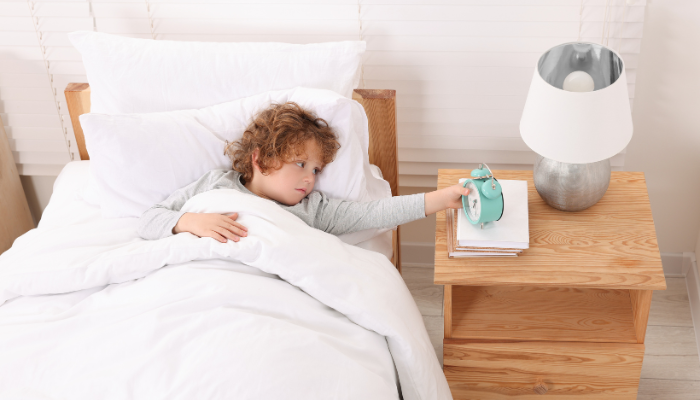 Little boy reaching to turn his alarm clock off for school.