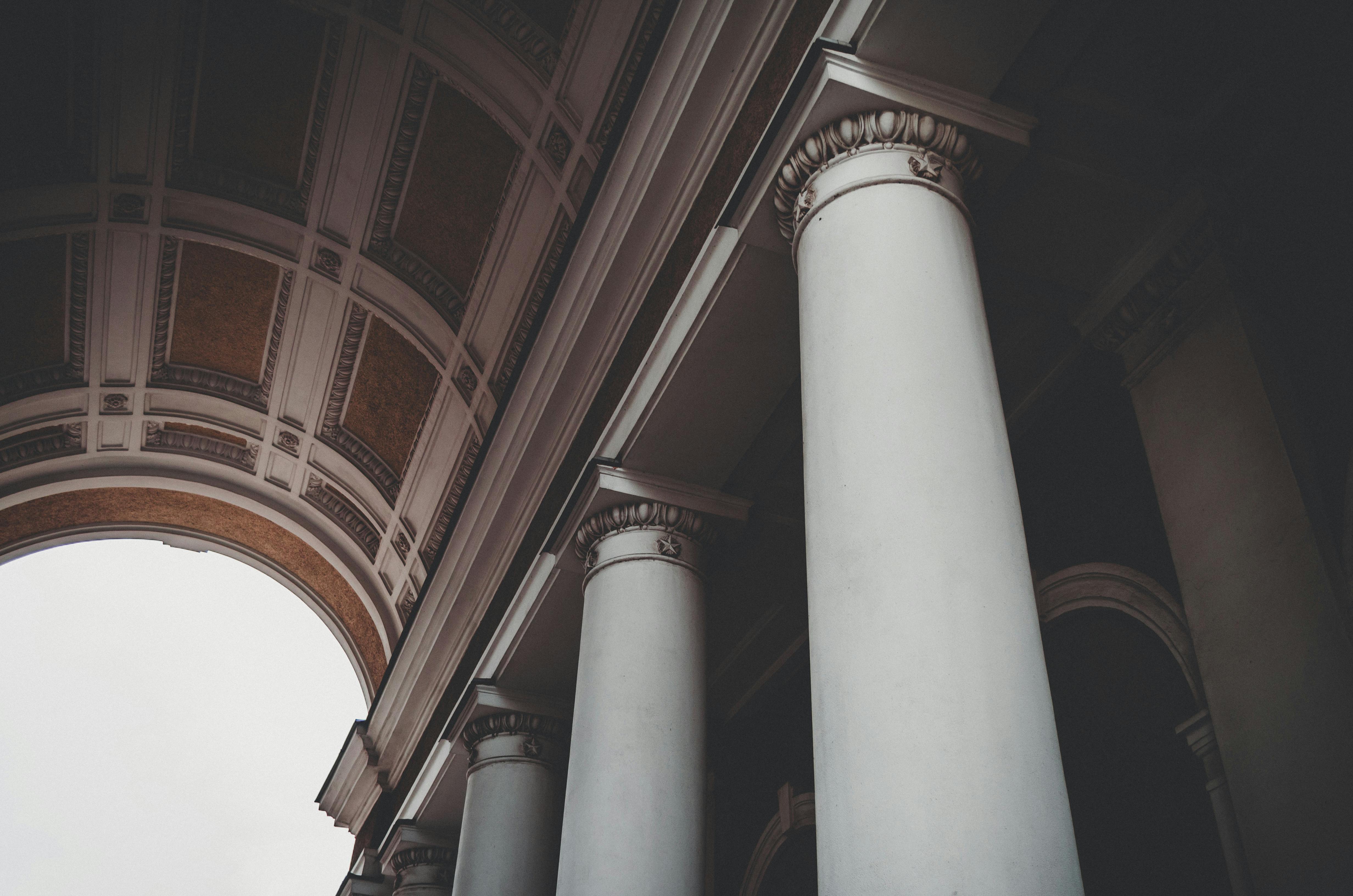 Upward view of classical white columns with ornate Corinthian capitals supporting a gold-inlaid ceiling. Symbolizes foundational strength, structure, and institutional authority—representing the five pillars of Digital Asset Entrepreneurship: creation, distribution, monetization, protection, and expansion.
