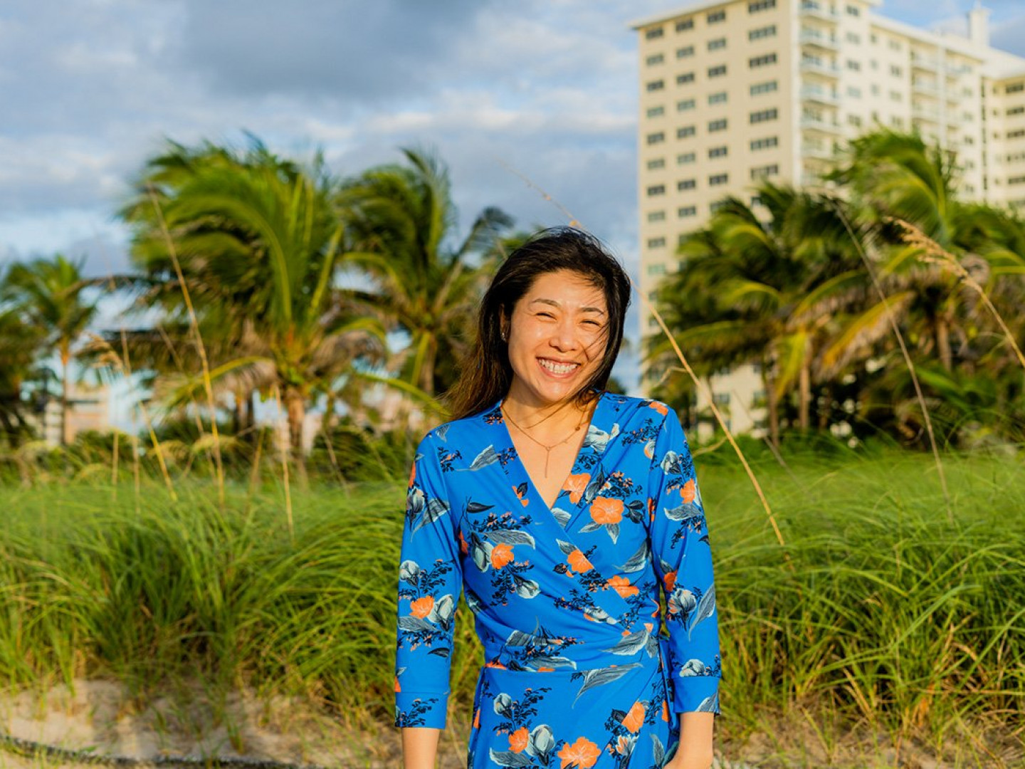 woman smiling at the camera with palm trees and a building in the background
