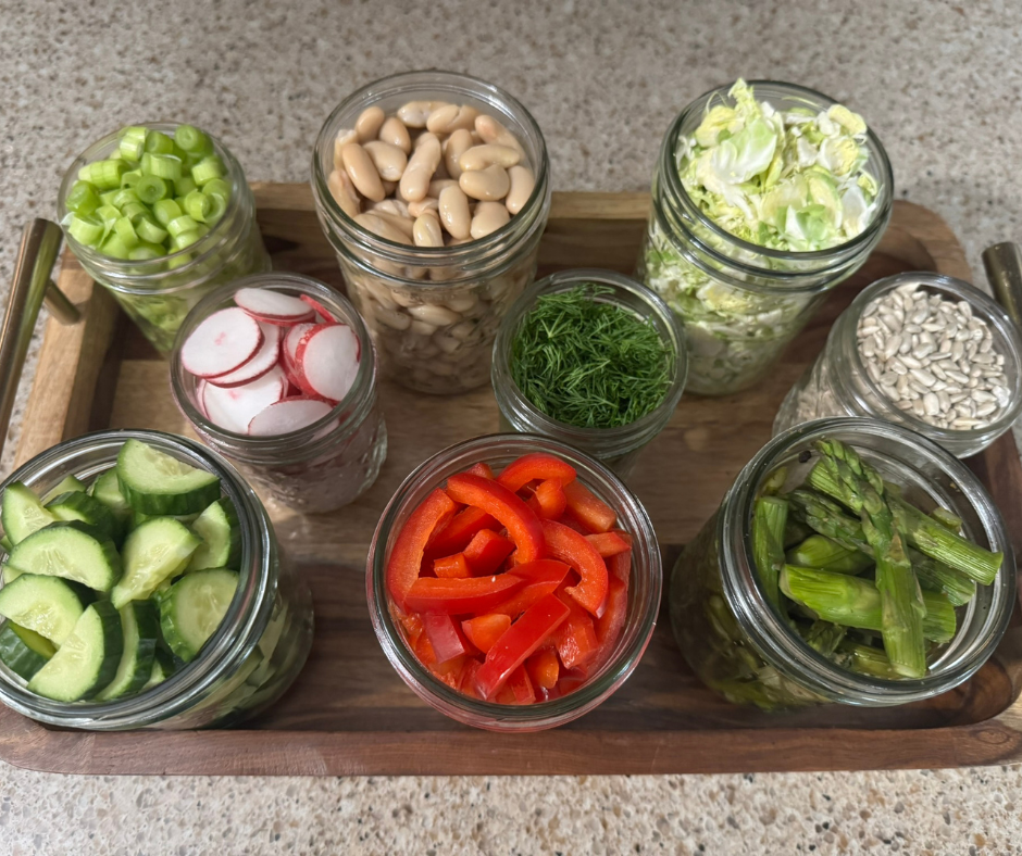 Prep-ahead salad ingredients arranged in jars for the Lemon-Dill Asparagus and White Bean Salad of the Week, including roasted asparagus, white beans, dill, and chopped vegetables.