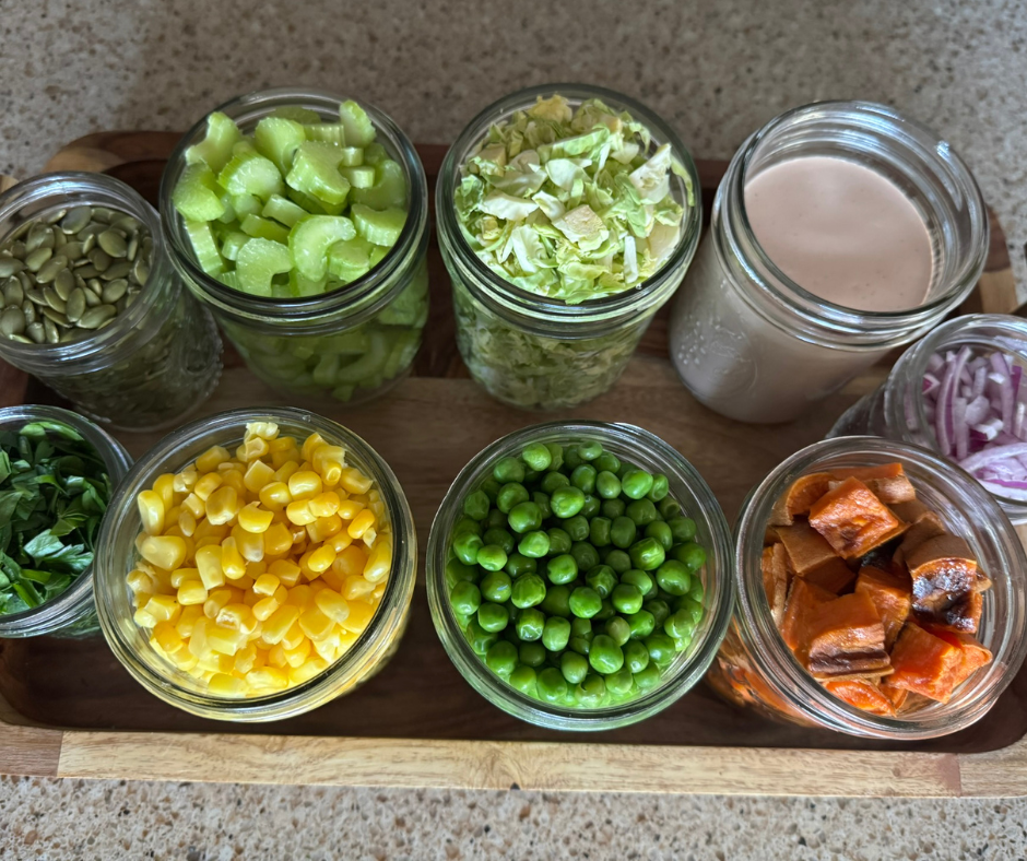 Prep jars with roasted sweet potatoes, peas, corn, Brussels sprouts, celery, red onion, parsley, and dressing for the sweet potato garden bowl