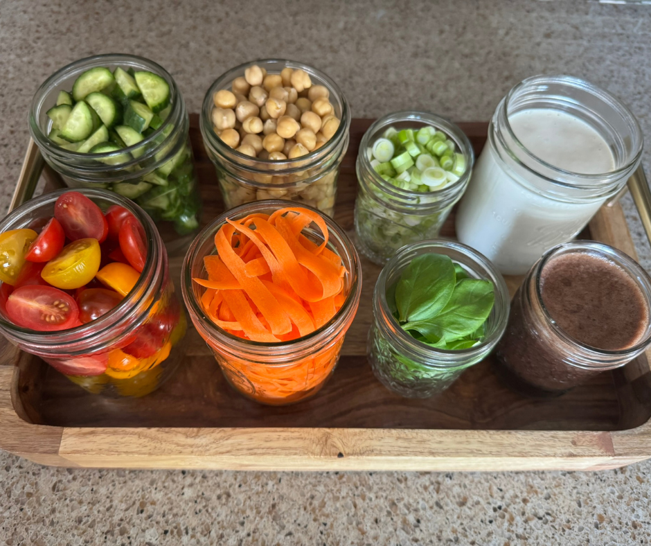 Prepped ingredients in jars for caprese-inspired salad including chickpeas, vegetables, and dressing