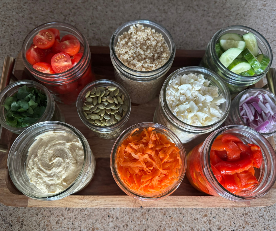 Prepared salad ingredients in jars including quinoa, vegetables, and hummus for easy meal prep