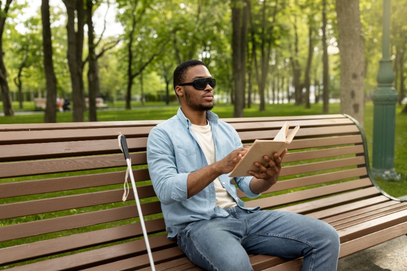young african-american sitting on park bench reading braille