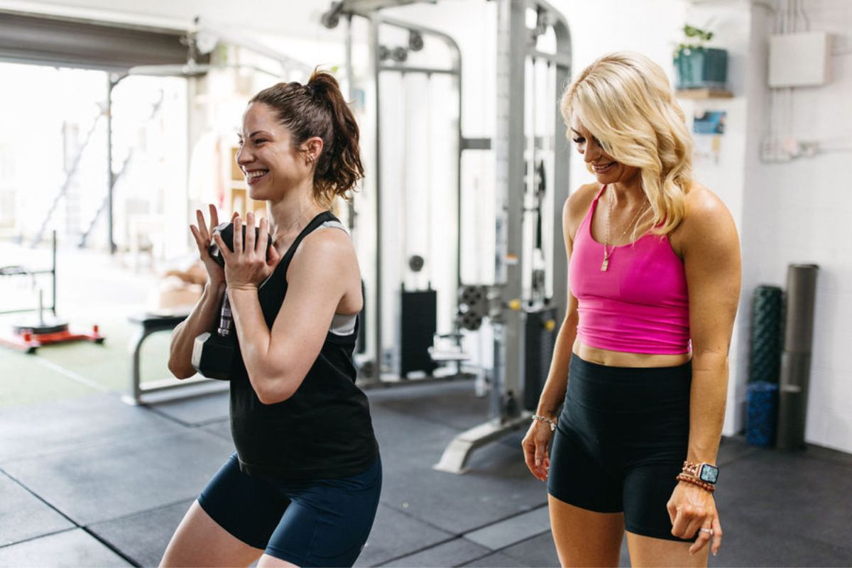 A pregnant woman holding a 7kg dumbbell about to squat with her 1:1 personal trainer as they train safely for both mum and baby at The Evolved All Female Gym in West End Brisbane