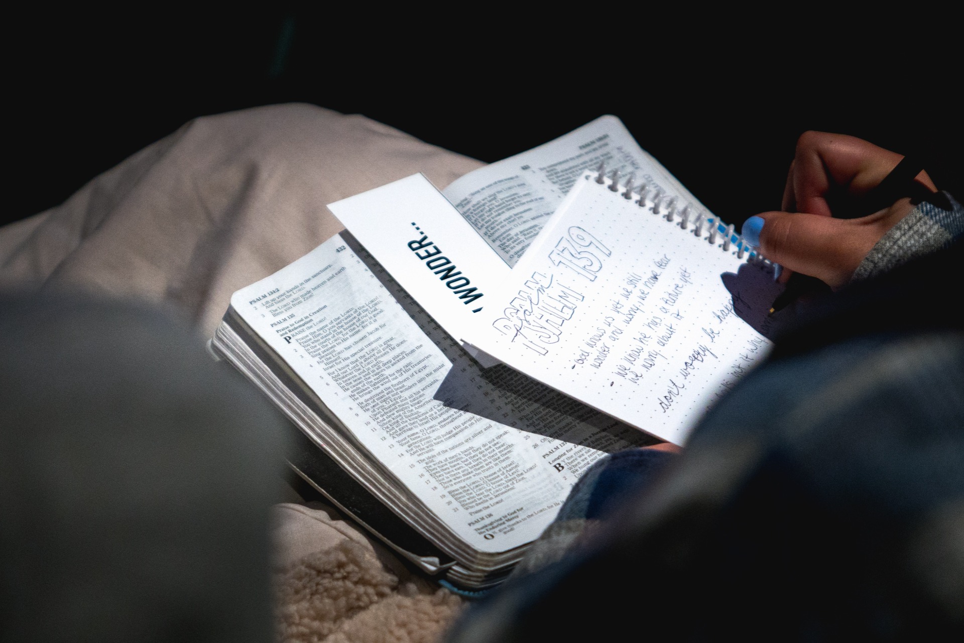 Someone writes notes on a pad on an open Bible