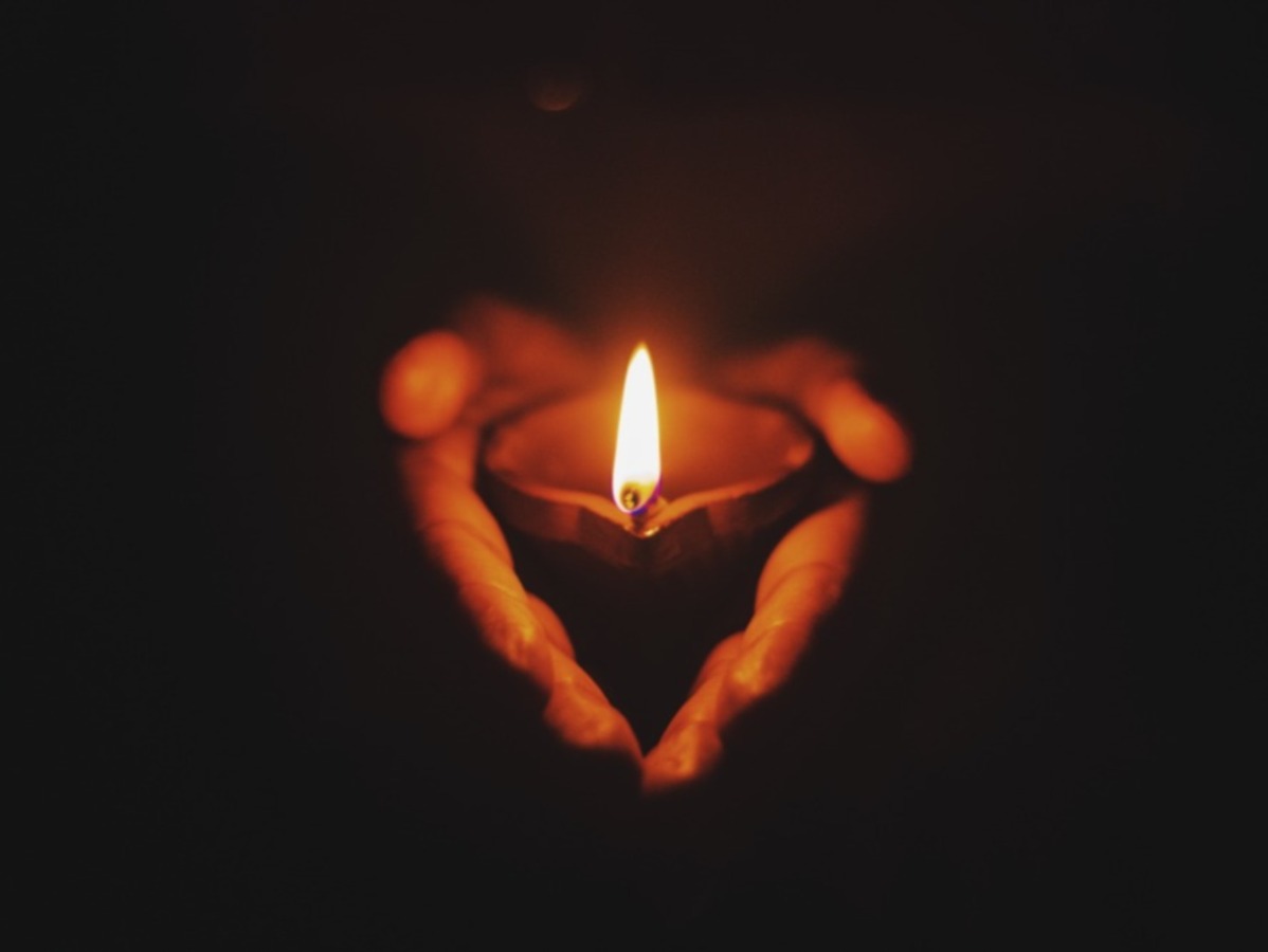 Hands hold a small lit candle