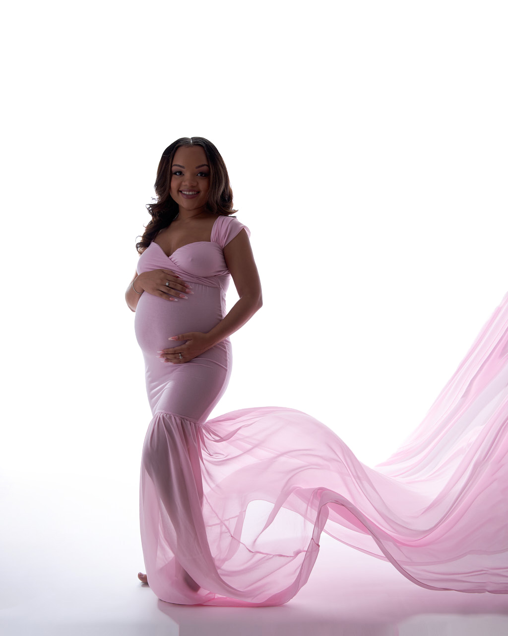 Modern Maternity Portrait of pregnant woman on white background in  flowing pink dress.